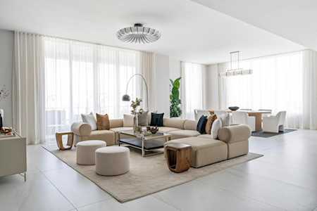Bright living room with cream sofas, round ottomans, and floor-to-ceiling windows.
