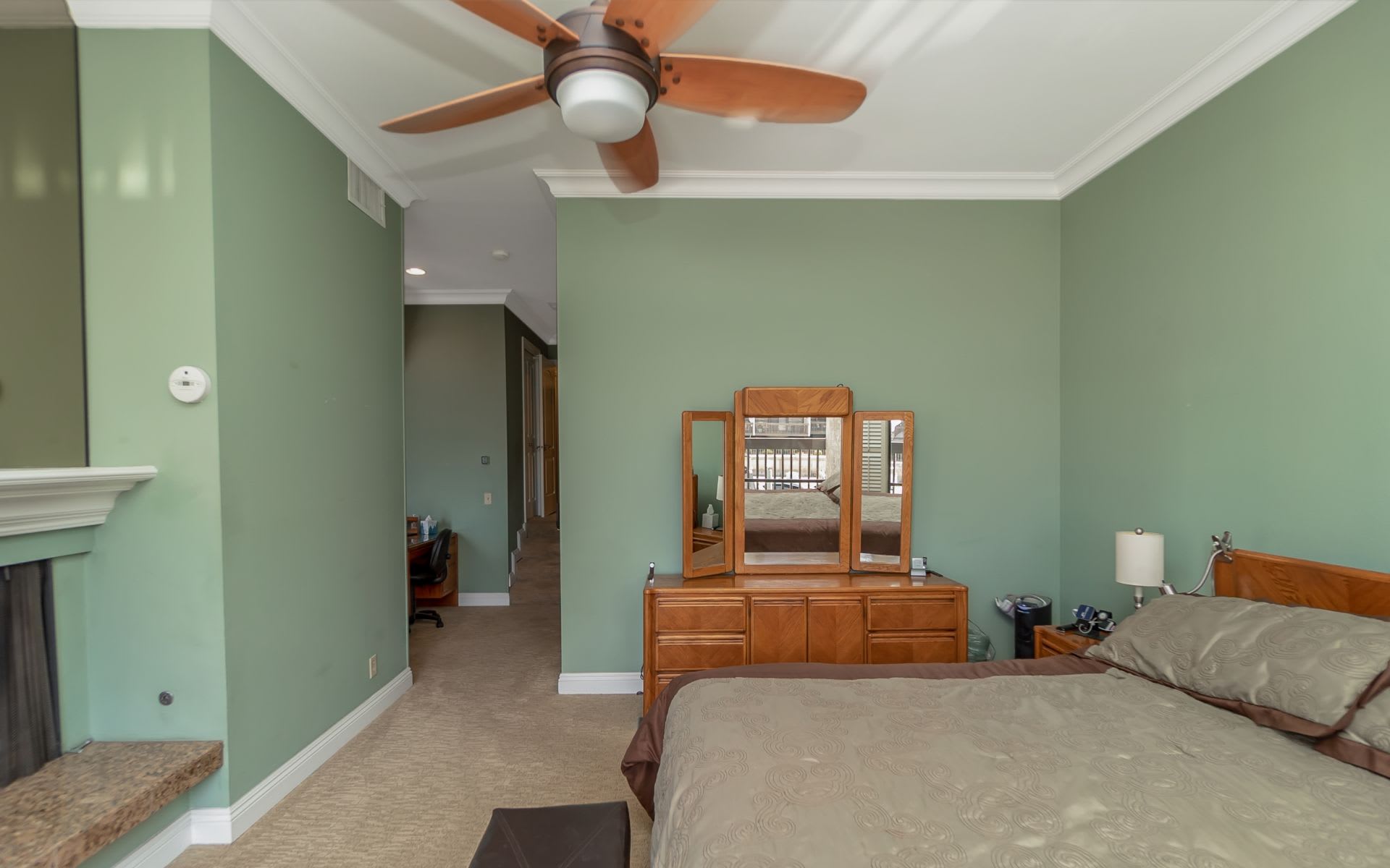 Bedroom with sage-green walls, a ceiling fan, fireplace, and wood dresser.