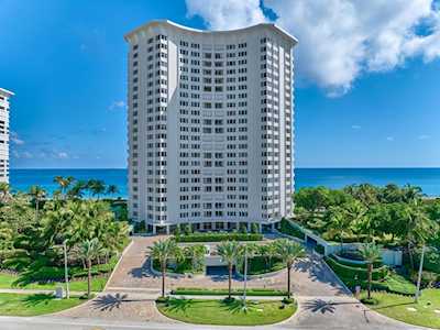 White oceanfront condominium tower framed by palm trees, with the Atlantic visible behind it.