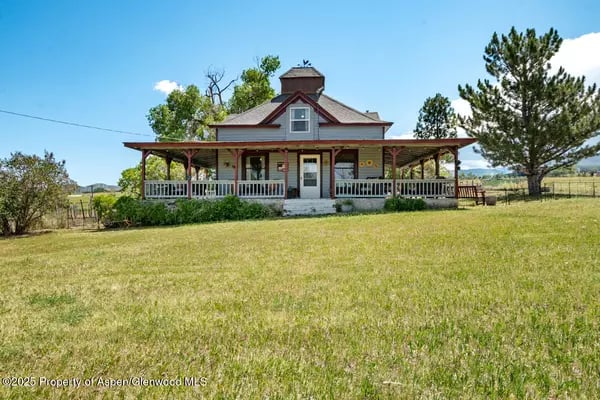 Rural farmhouse with a wraparound porch beyond a broad grassy lawn.