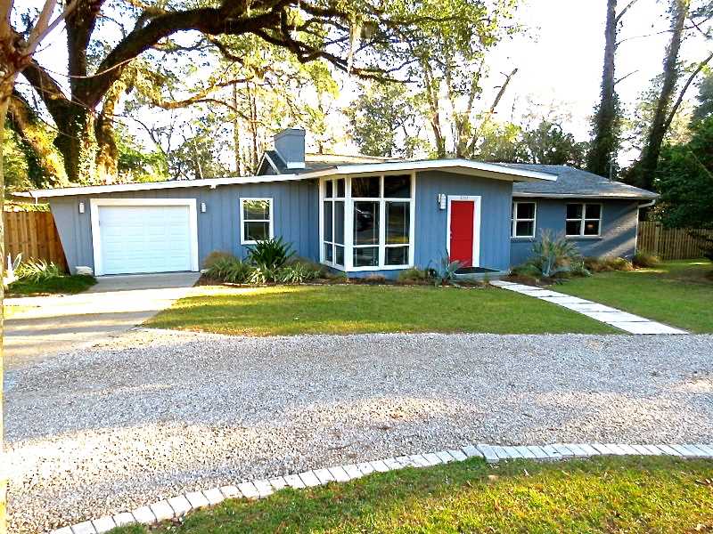 A blue house featuring a red door and a driveway, set against a clear sky.