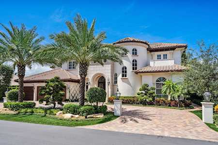 Two-story stucco home with a tile roof, arched entry, palms, and landscaped front yard.
