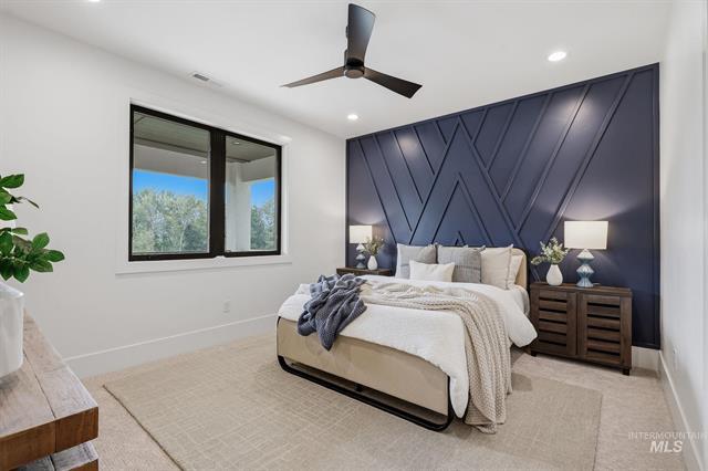 Staged bedroom with a geometric navy accent wall, white bedding, and a window overlooking trees.