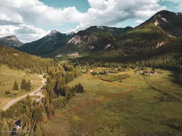 Aerial view of a red-outlined meadow parcel beneath forested mountains.