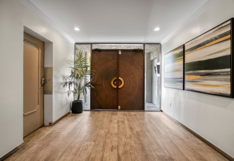 Apartment entry foyer with carved wooden double doors, light wood flooring, and abstract wall art.
