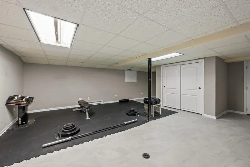 Basement exercise room with weightlifting equipment, black gym flooring, and white double doors.