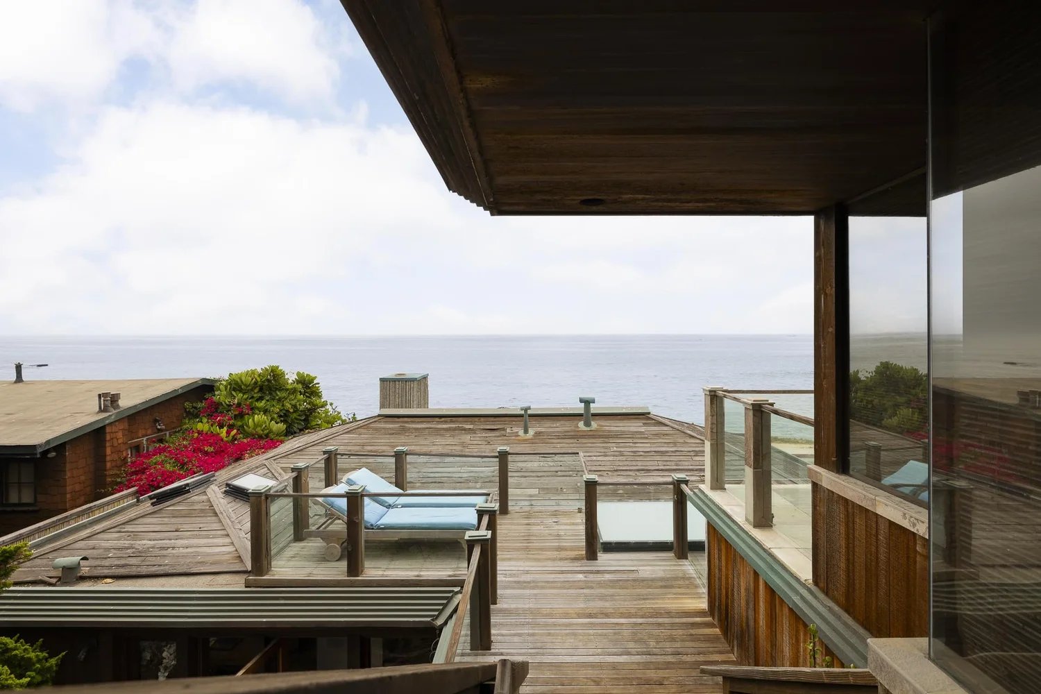 Wood rooftop deck of the Kravis Residence with lounge chairs and a view over neighboring roofs to the Pacific Ocean.