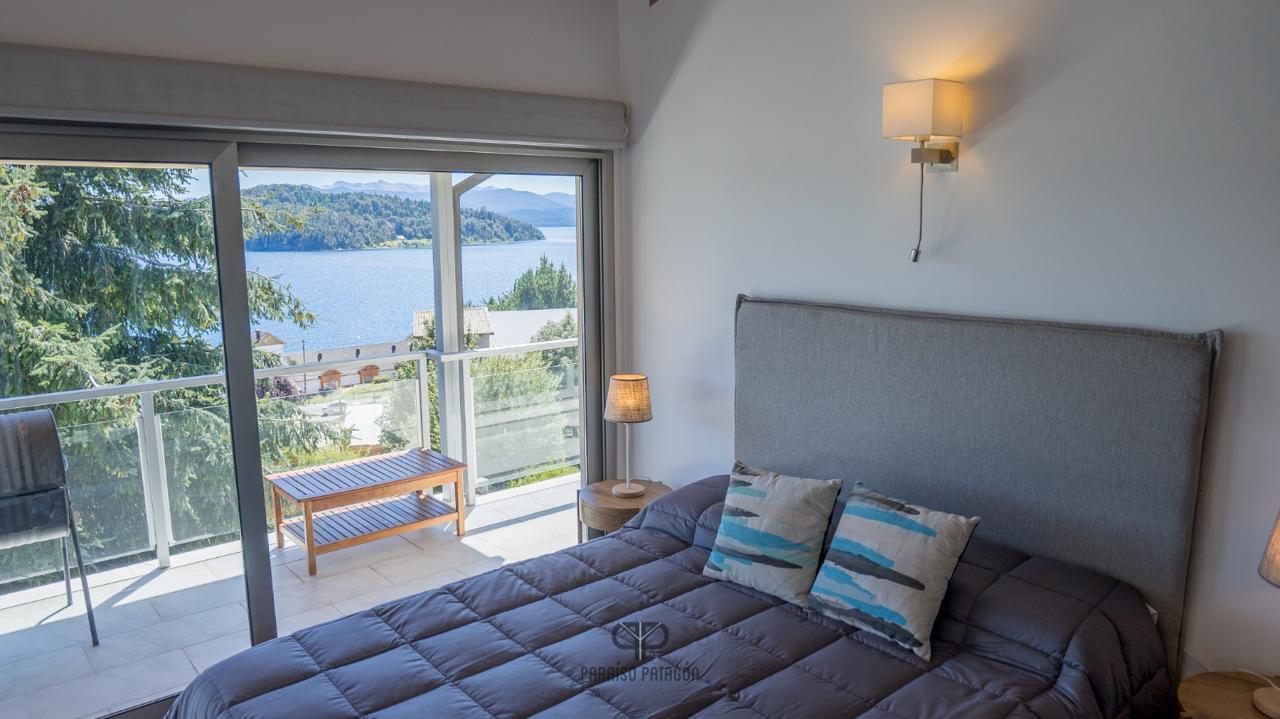 Furnished bedroom with sliding glass doors overlooking a lake and wooded mountains.