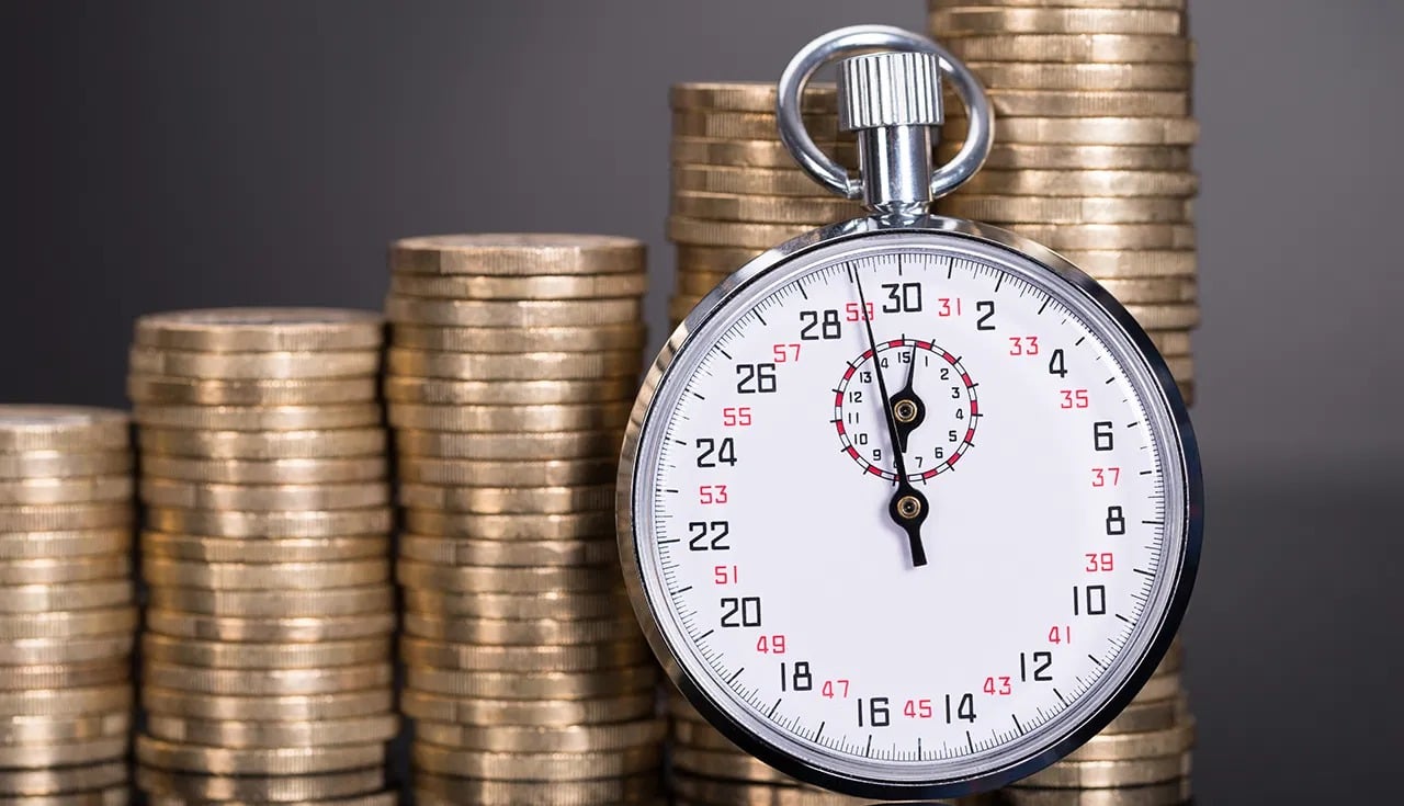 A stopwatch stands before ascending stacks of coins.