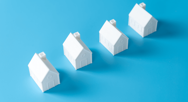 An image of small white house models on a blue background, suggesting themes of real estate, property investment, or housing market analysis.