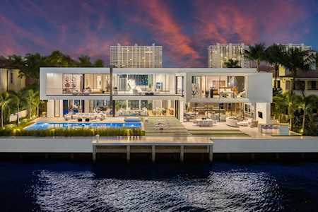 Contemporary waterfront home with a lit pool and glass walls at dusk.