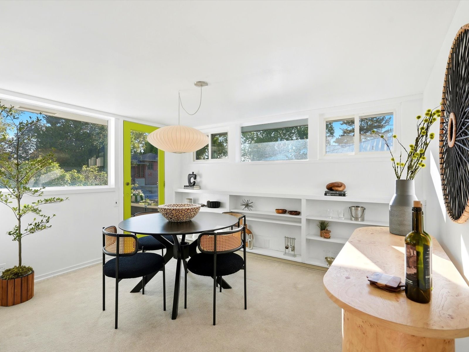 Bright dining room with a round black table, built-in shelving, and a vivid lime-green door.