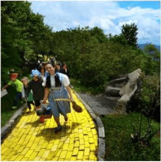 People walk along a bright yellow brick path through a wooded outdoor area.