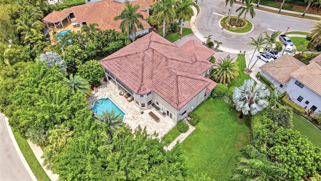 Aerial view of a tile-roofed home with a curved pool, tropical landscaping, and a large lawn.