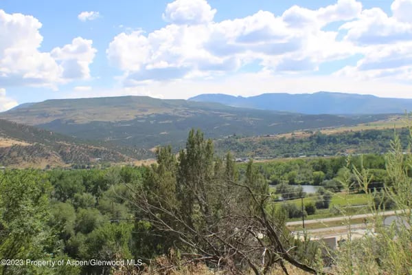 Mountain valley near Rifle, with green trees in the foreground and layered hills beneath a cloudy blue sky.