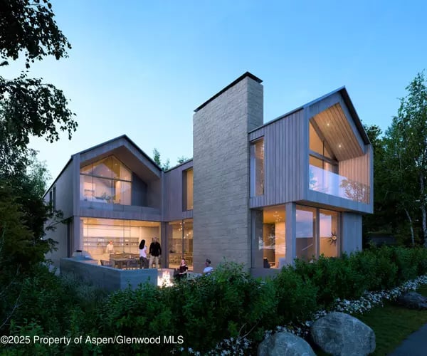 Modern home with expansive windows and a tall stone chimney, surrounded by landscaped grounds at dusk.