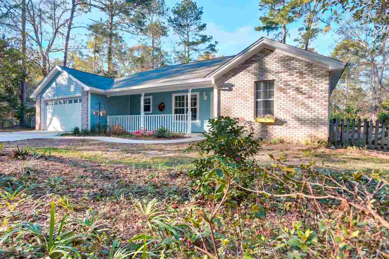 A blue house nestled in a wooded area, surrounded by lush trees and vibrant shrubs.