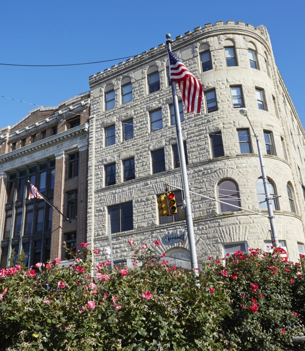 Light-stone building with a rounded corner, American flag, and pink roses in the foreground.