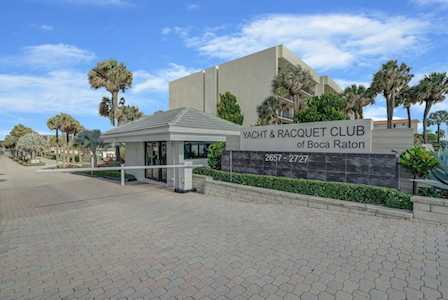 Yacht & Racquet Club of Boca Raton entrance, with a stone sign, guard gate, palms, and paved driveway.