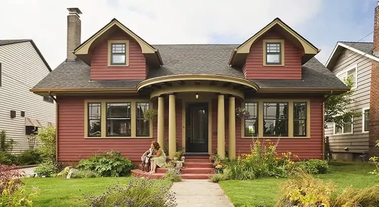 A picturesque red house with a well-kept garden and lawn. The house has a traditional design with a porch and large windows. This scene evokes a sense of homeliness and comfort.