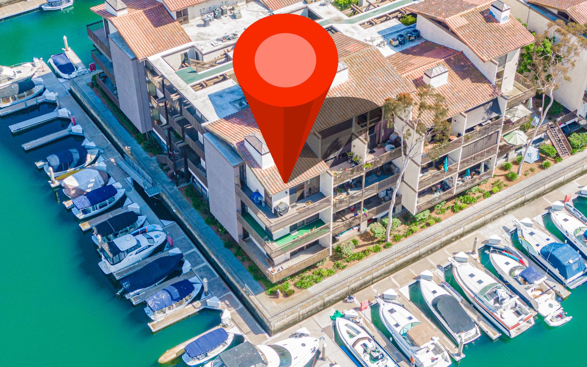 Waterfront condominiums beside marina docks, with boats and a red location marker.