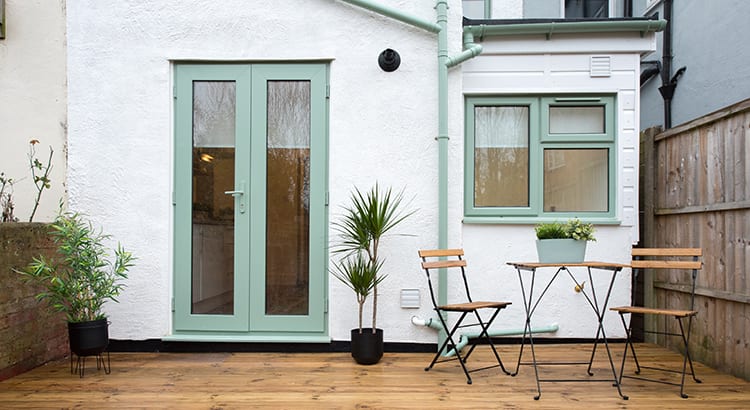An outdoor patio area with double doors leading inside. There are potted plants and a small table with chairs, creating a cozy outdoor living space.