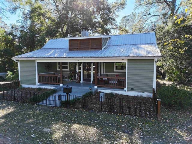 A charming house in 825 E Dogwood with a spacious front porch, situated on a slightly elevated lot. The yard is well-kept with some landscaping, and the house is surrounded by trees, giving it a cozy and inviting feel.