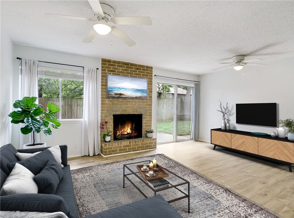 Staged living room with a brick fireplace, lit fire, and sliding glass doors.