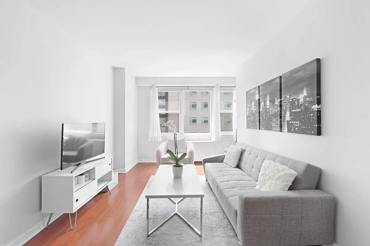 Living room with a gray sofa, white coffee table, and large windows overlooking nearby buildings.