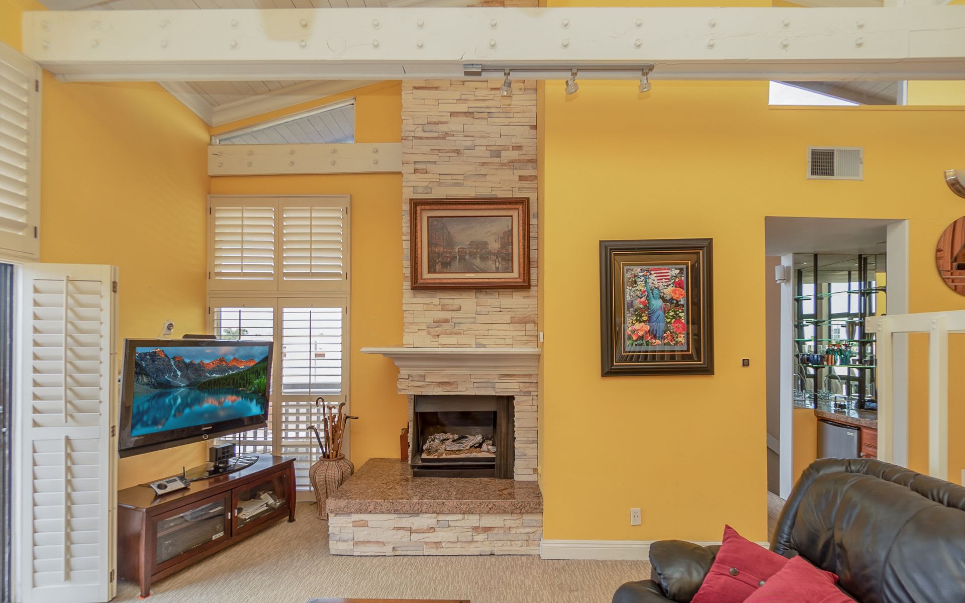 Living room with a stone fireplace, yellow walls, plantation shutters, and a leather sofa.
