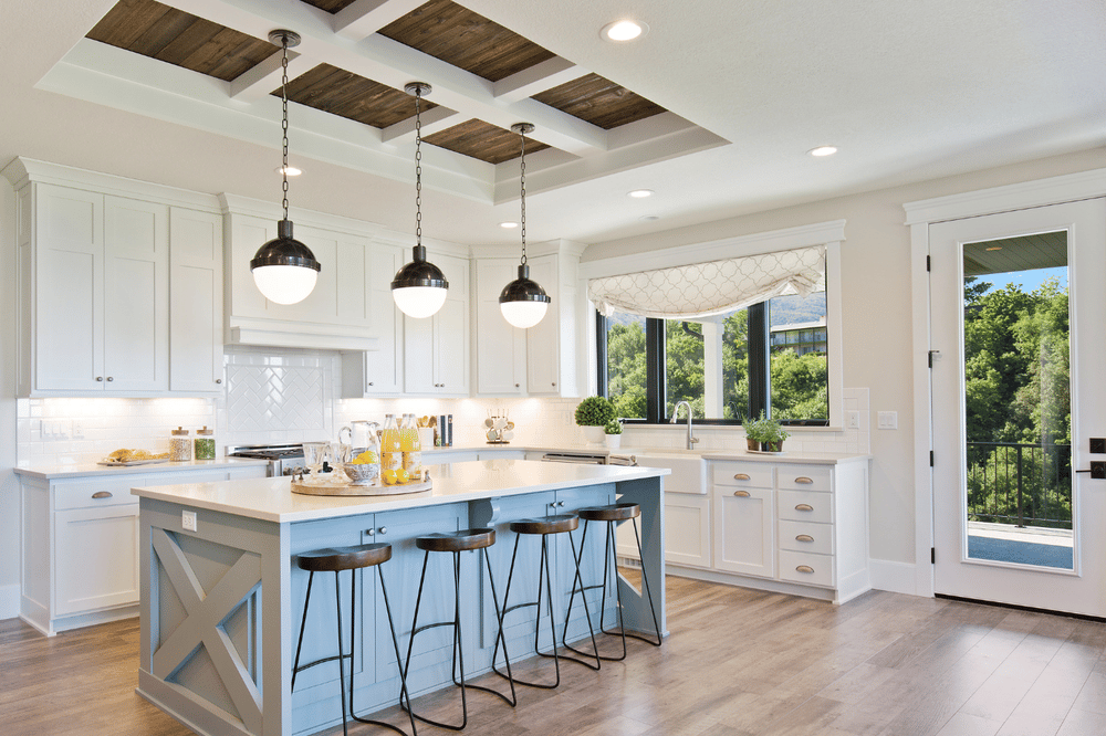 Bright kitchen with white cabinets, a pale blue island, pendant lights, and wooded views.