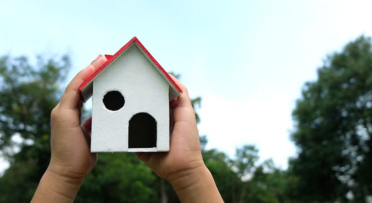A person holding a small model house in their hands, symbolizing homeownership, care, or protection of property.