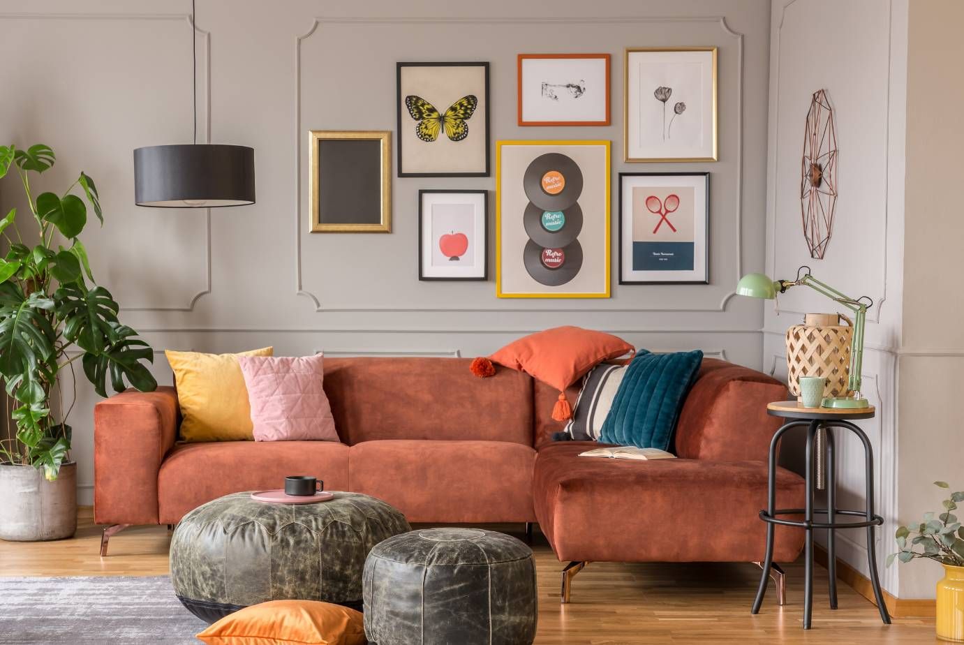 Living room with a rust-colored sectional, colorful cushions, framed artwork, and potted plants.