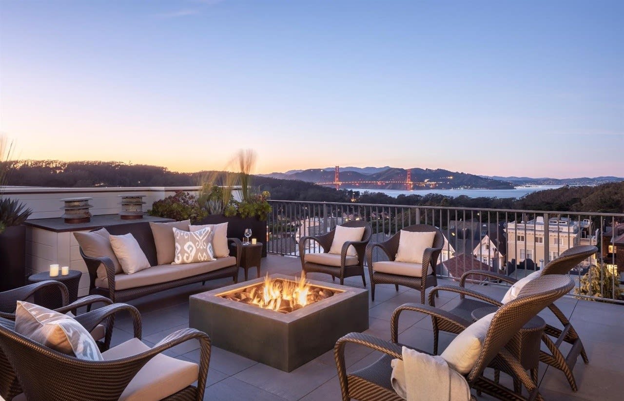 Outdoor patio with fire pit, wicker seating, and views of the Golden Gate Bridge at sunset.