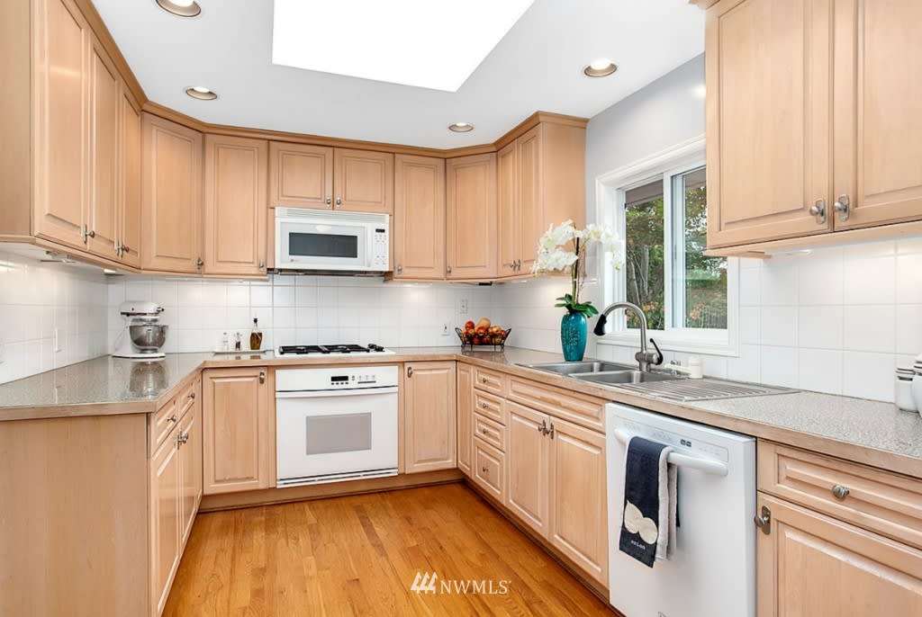 Kitchen with light wood cabinetry, hardwood floors, and a sink beneath a window.