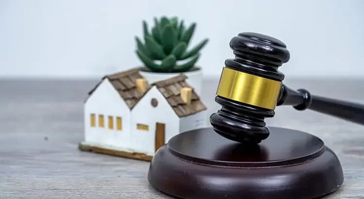 A small model house with a gavel, placed on a table. This image likely represents real estate transactions, property law, or legal matters related to housing.