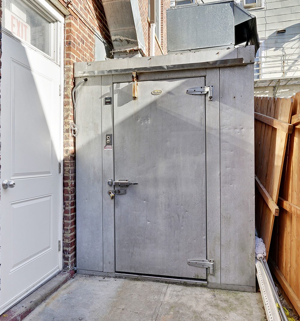 Building service area with a large metal walk-in cooler beside an exit door.