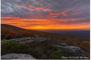 Autumn mountain ridges at sunset, viewed from a rocky overlook with a wooden fence.