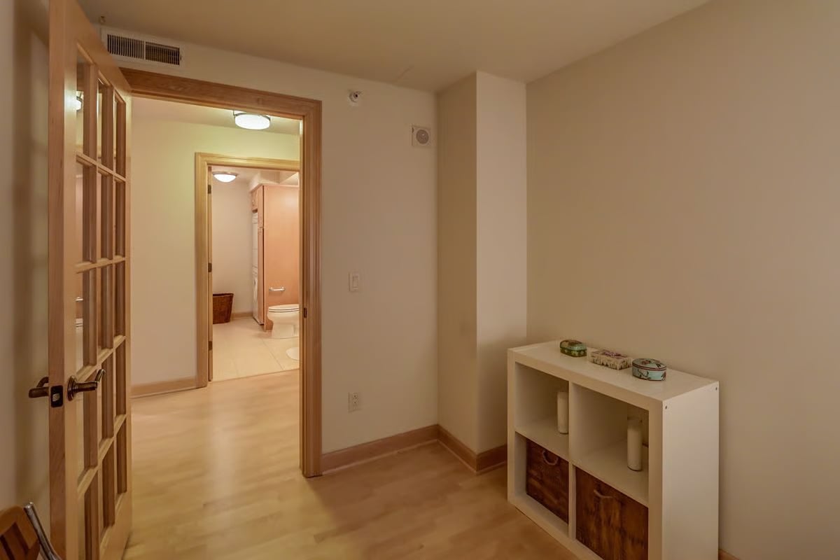 Hallway with an open glass-paneled wooden door and a bathroom visible beyond.