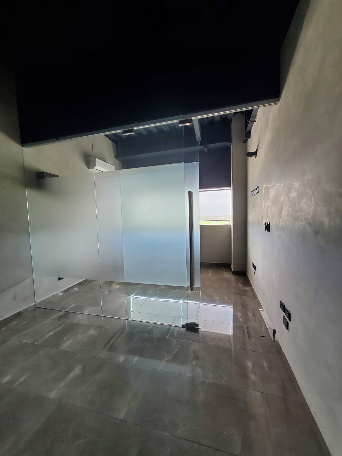 Vacant office with a glass partition, frosted panels, and gray tiled floors.