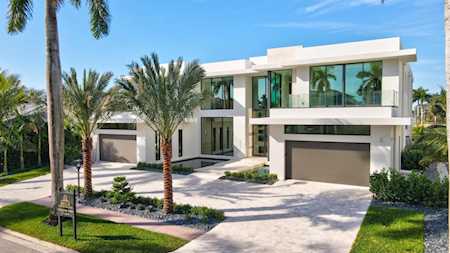 Modern white two-story home with expansive glass windows, a double garage, and palm-lined driveway.