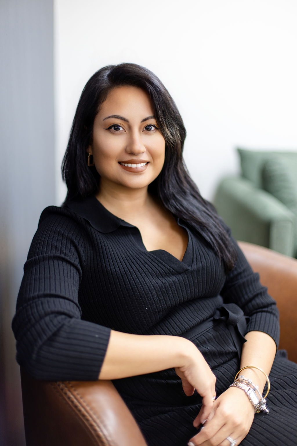 Karol Jaimes seated in a brown leather chair, wearing a black ribbed outfit.