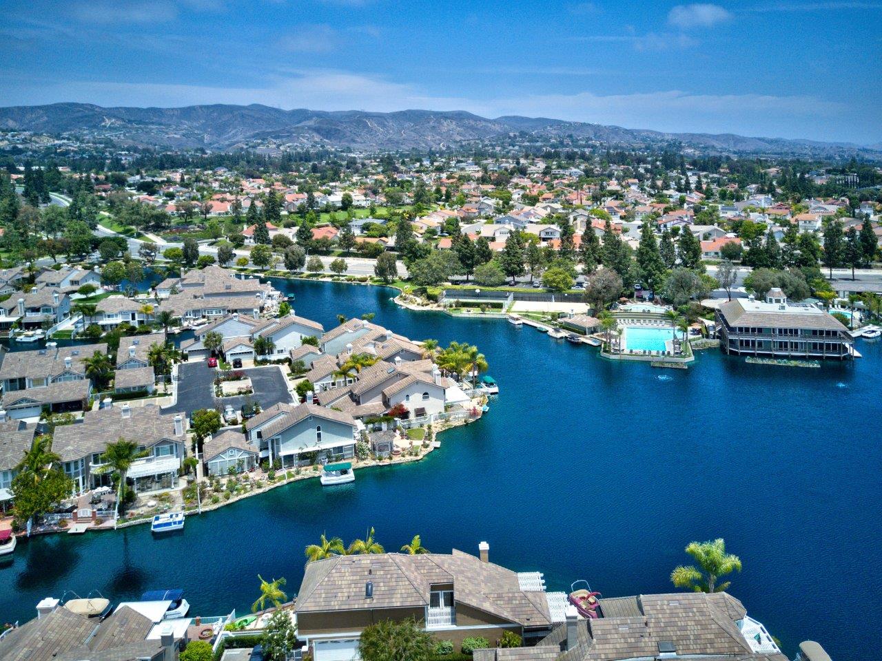 Aerial view of waterfront homes along a lake, with a community pool and hills beyond.