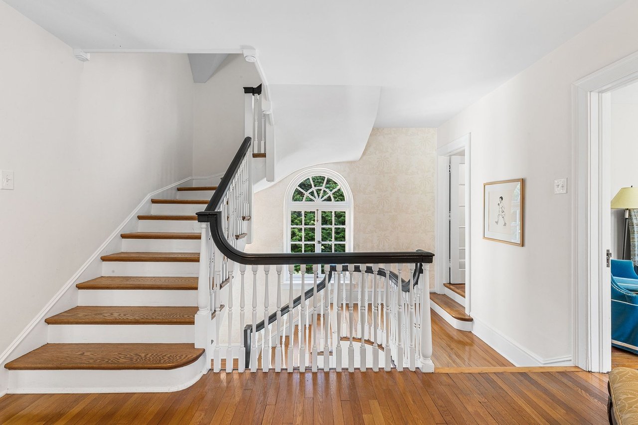 Wooden staircase and landing with a dark handrail and arched window.