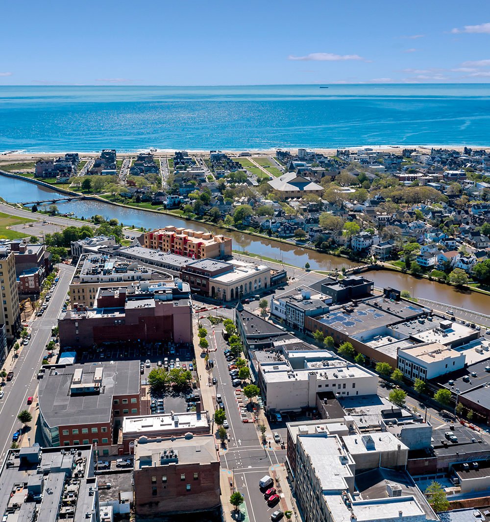 Aerial view of coastal downtown buildings, a waterway, beachfront homes, and the ocean.