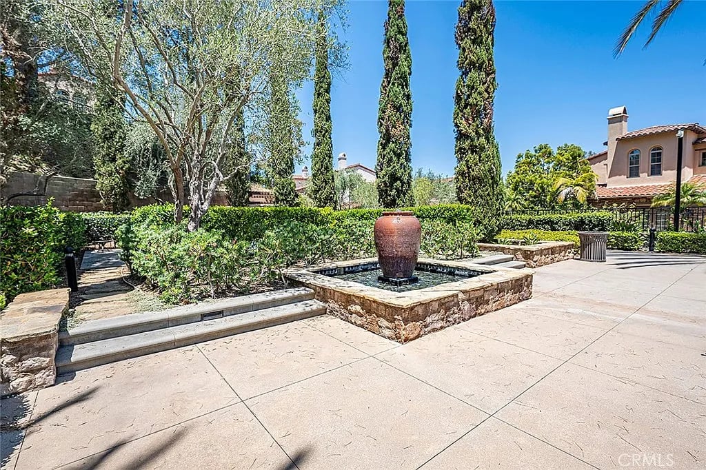 Landscaped courtyard with a stone fountain, clipped hedges, and tall cypress trees.