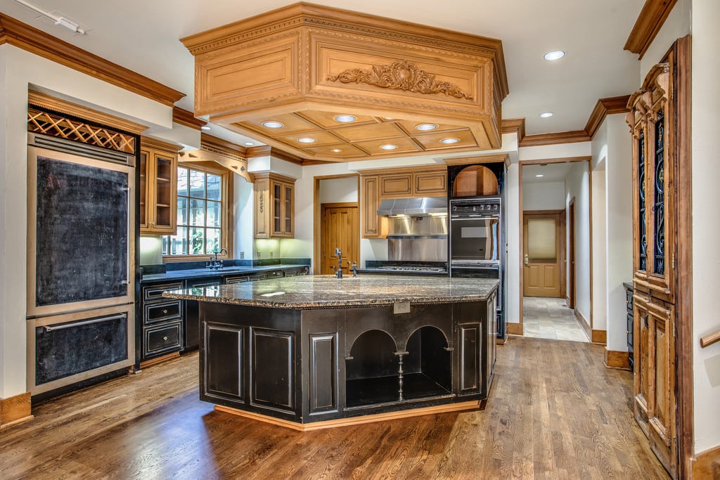 Ornate kitchen with a large dark island, carved wood ceiling, and extensive built-in cabinetry.