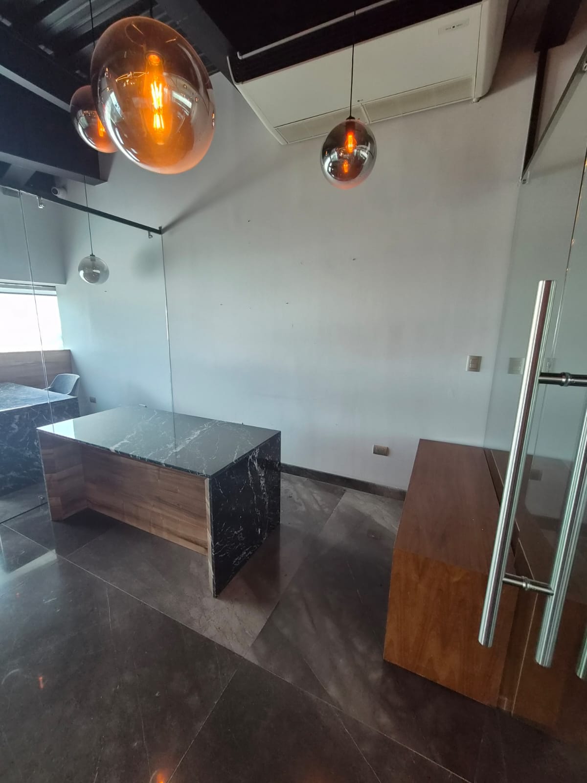 Office reception area with a marble-topped desk, glass partition, and orange pendant lights.