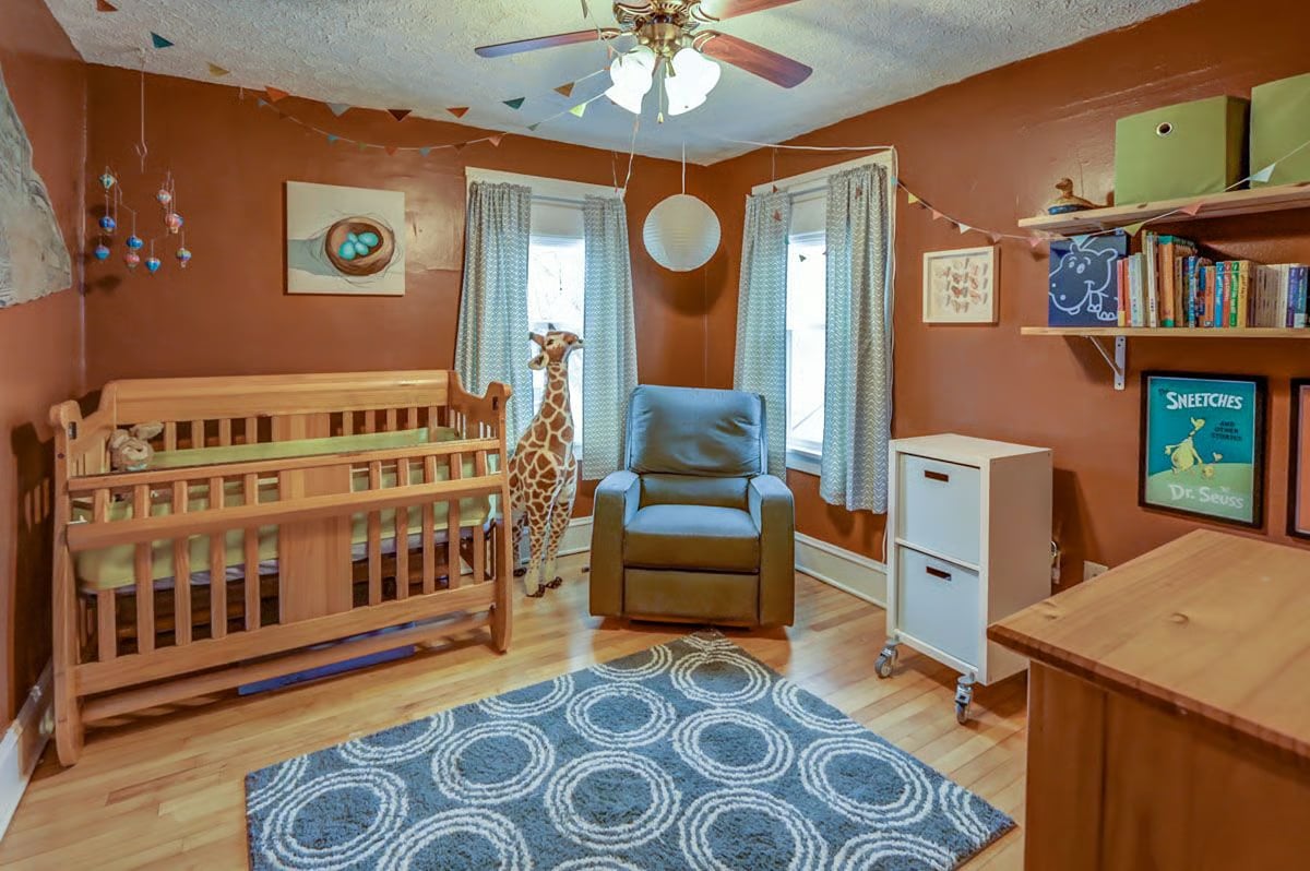 Nursery with a wooden crib, blue glider, giraffe toy, and patterned rug.