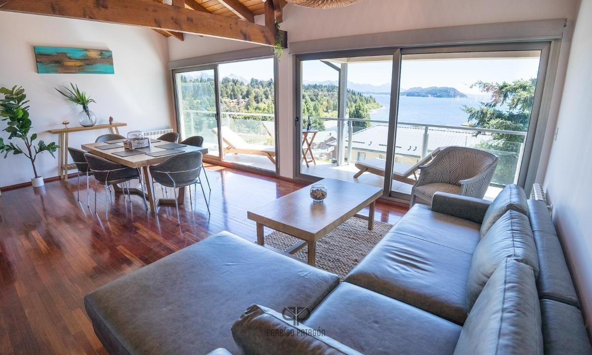 Furnished apartment living and dining room with a gray sectional and wide lake views from the balcony doors.